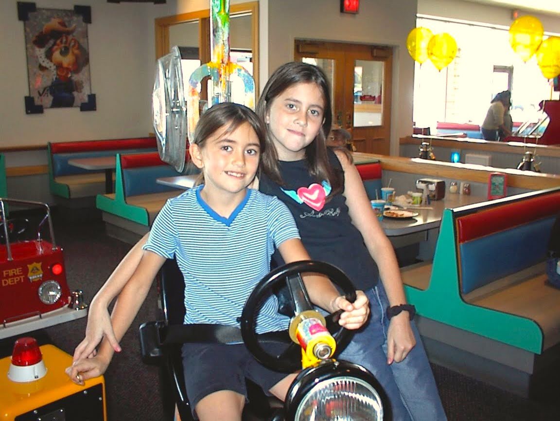 Kim and Christina sitting together on an arcade fire-truck ride at Chuck E. Cheese, early 2000s