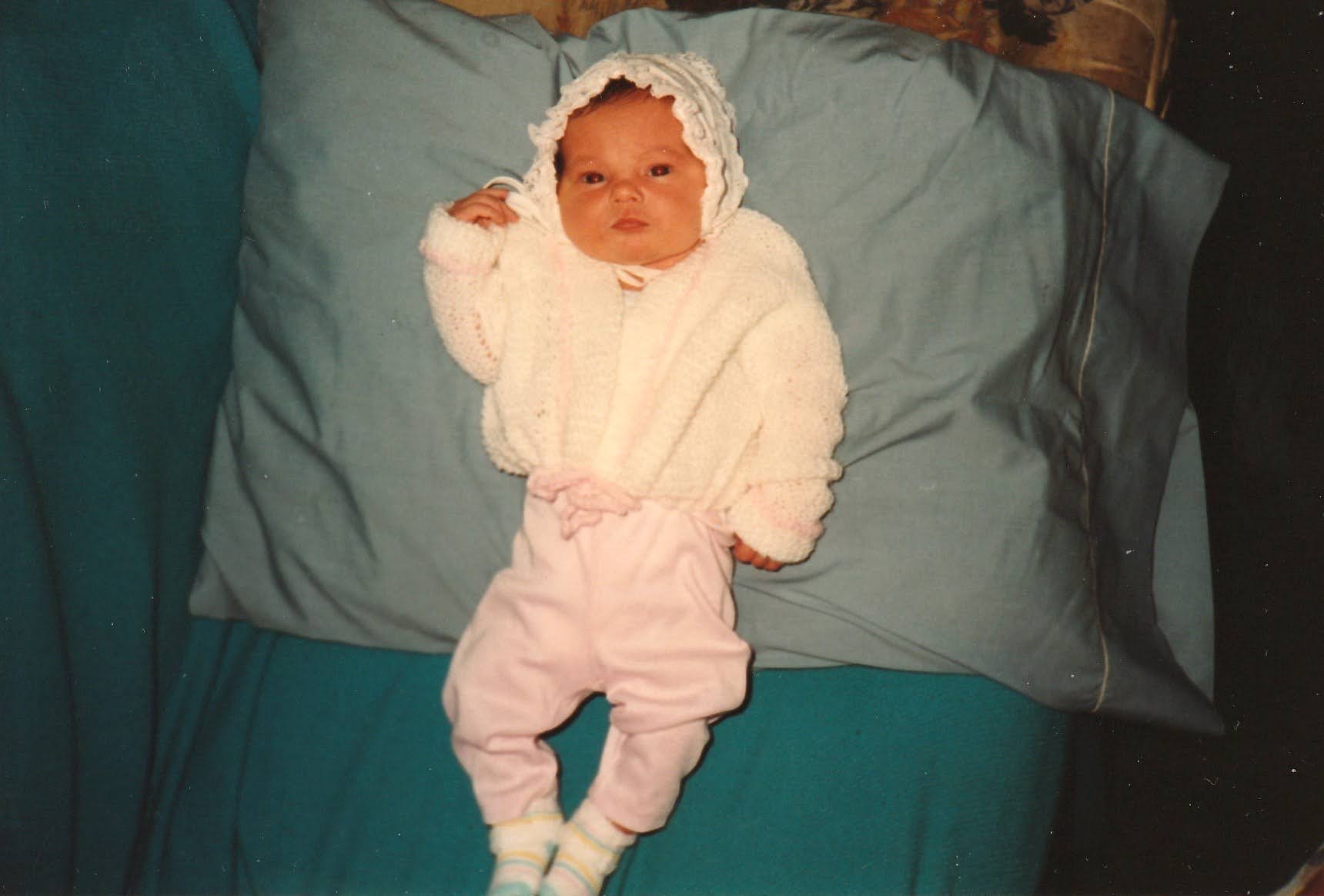 Newborn Kim in a knit white bonnet and sweater on a blue pillow, 1994