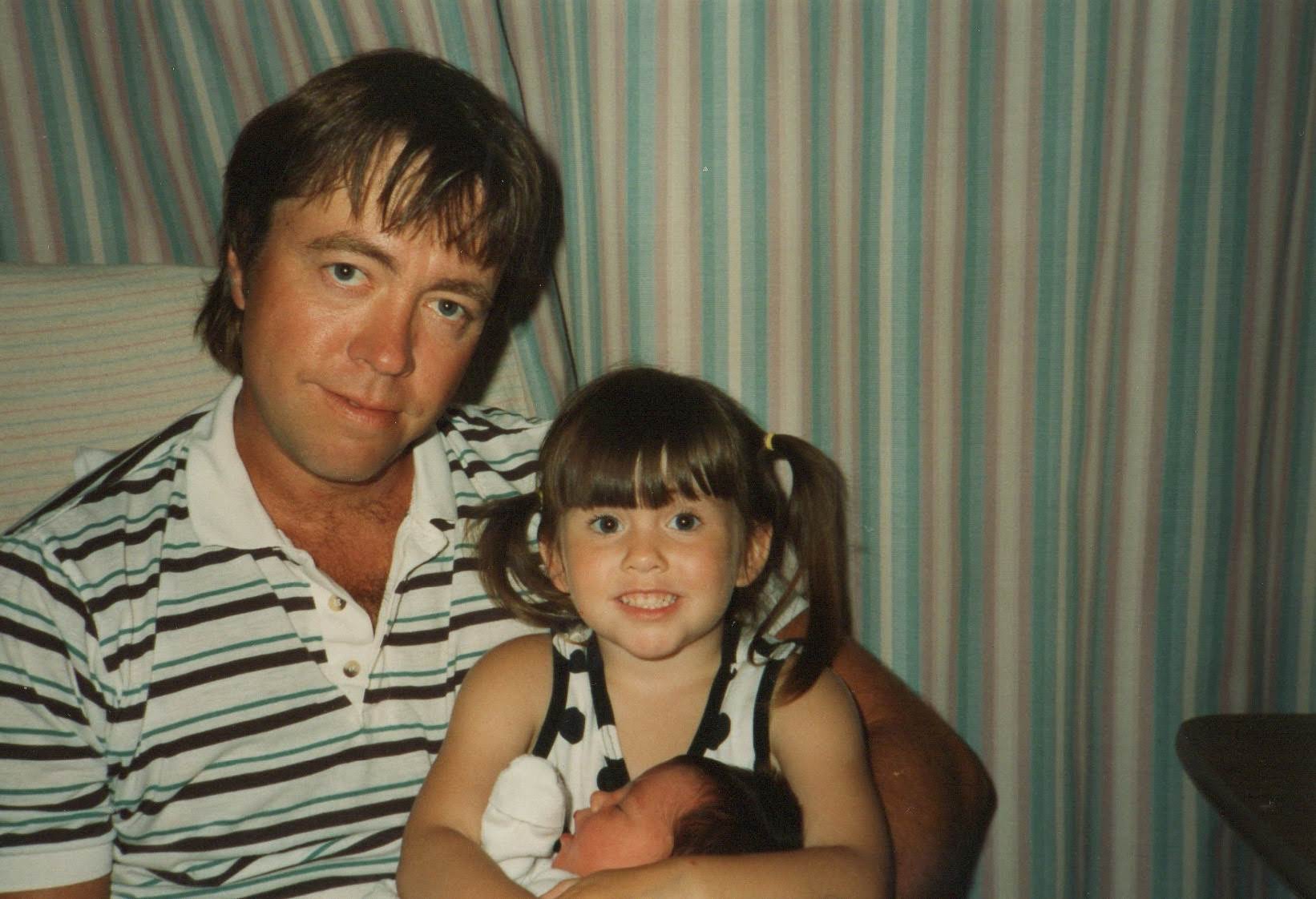 Larry in a striped polo holding baby Kim with Christina on his lap, 1994