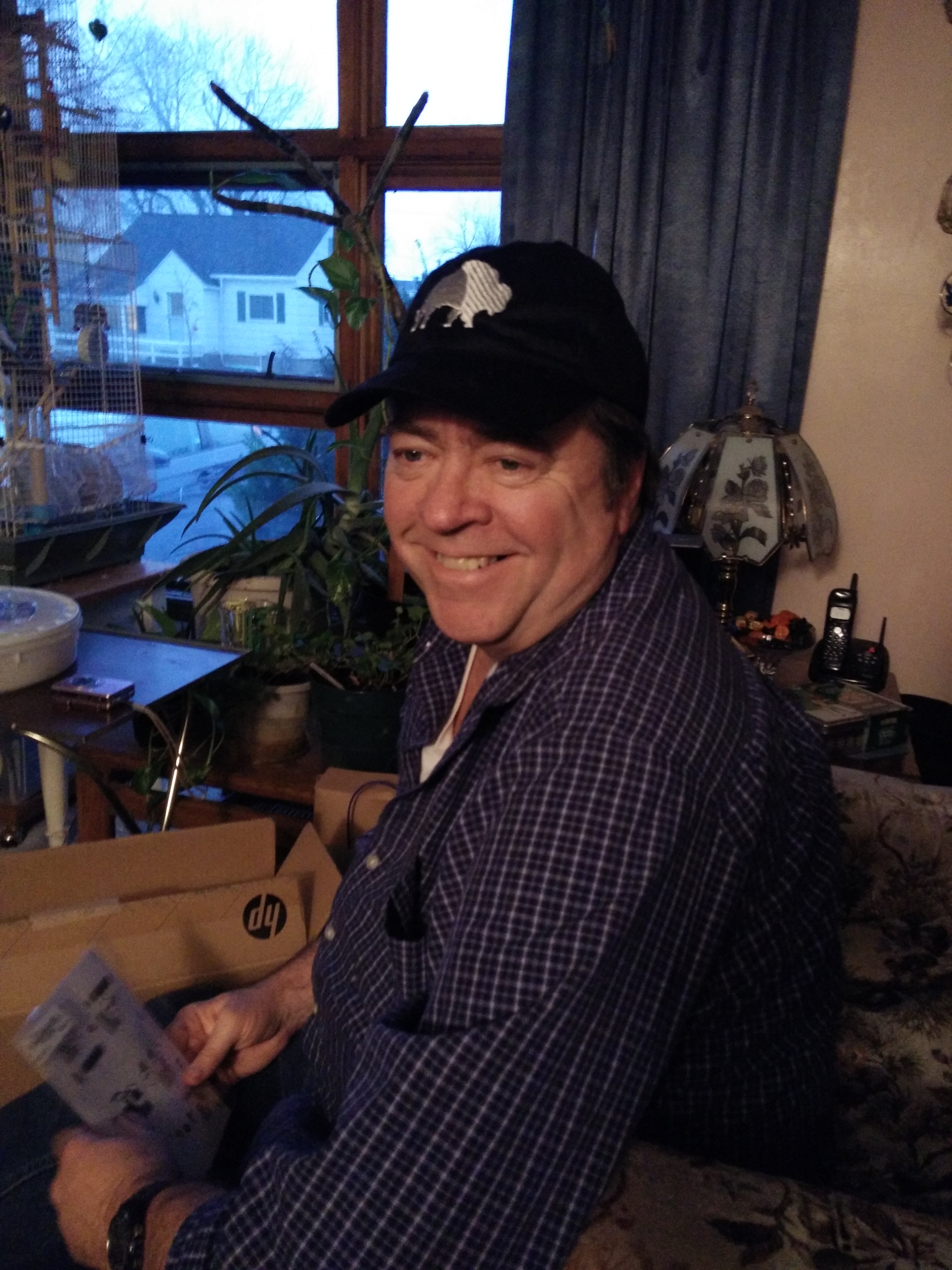 Larry in a Buffalo cap, smiling, opening an HP box on Christmas Eve at the Cheektowaga family home, 2016