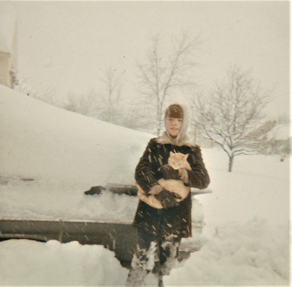 Larry in a winter coat holding an orange tabby cat in the snow, 1966