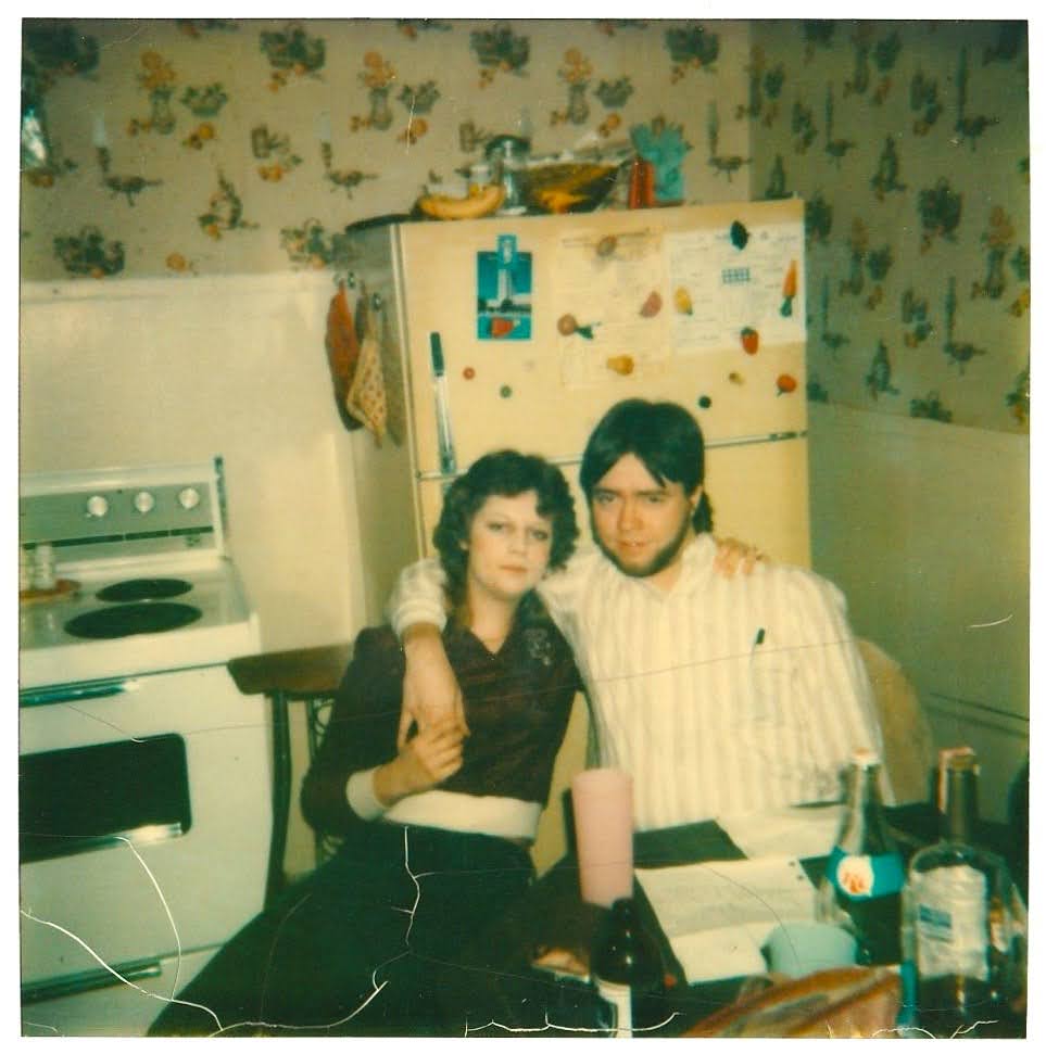 Larry and Jan in a kitchen with floral wallpaper