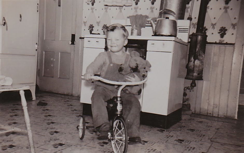 Mike on his tricycle in the family kitchen, holding a teddy bear