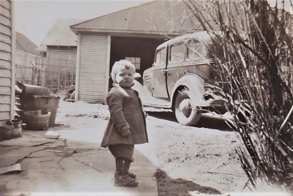 Mike as a toddler in a winter coat by the family car